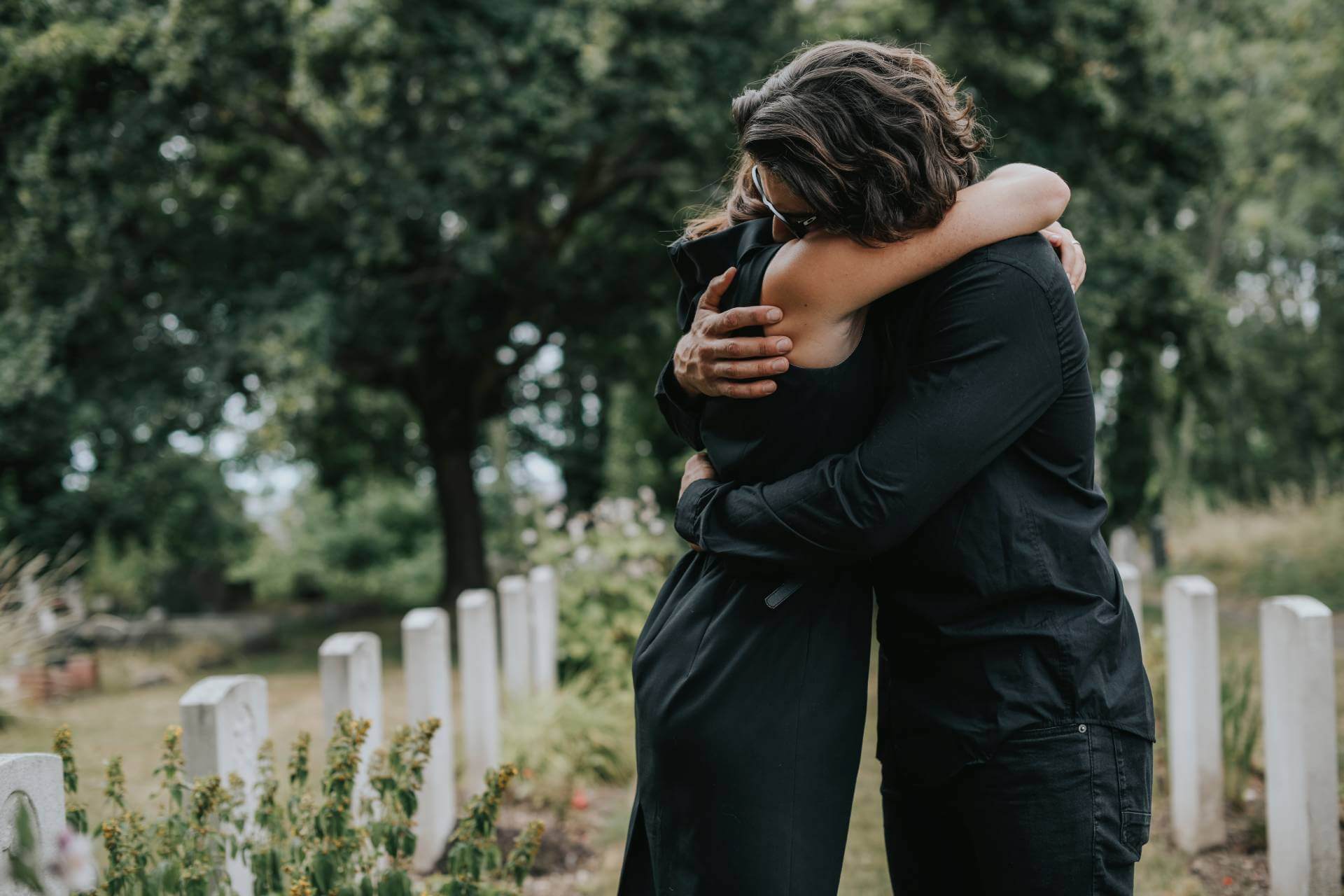 Couple wearing black consoling one another at cemetery