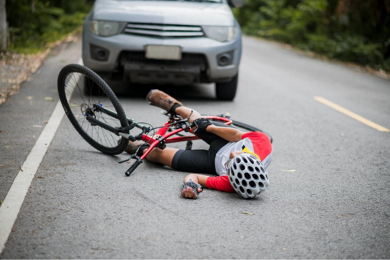 A cyclist is lying on the road after a bicycle accident with a car